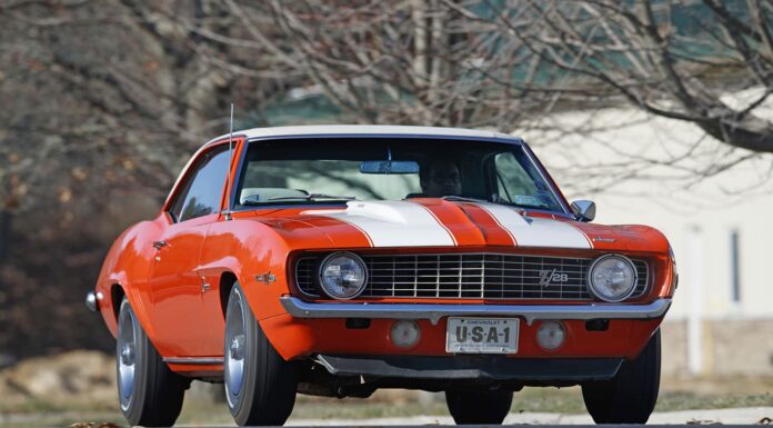 Low-angle front shot of an original Hugger Orange 1969 Chevrolet Camaro Z/28 with white racing stripes, cowl induction hood, and USA-1 front novelty plate on asphalt.