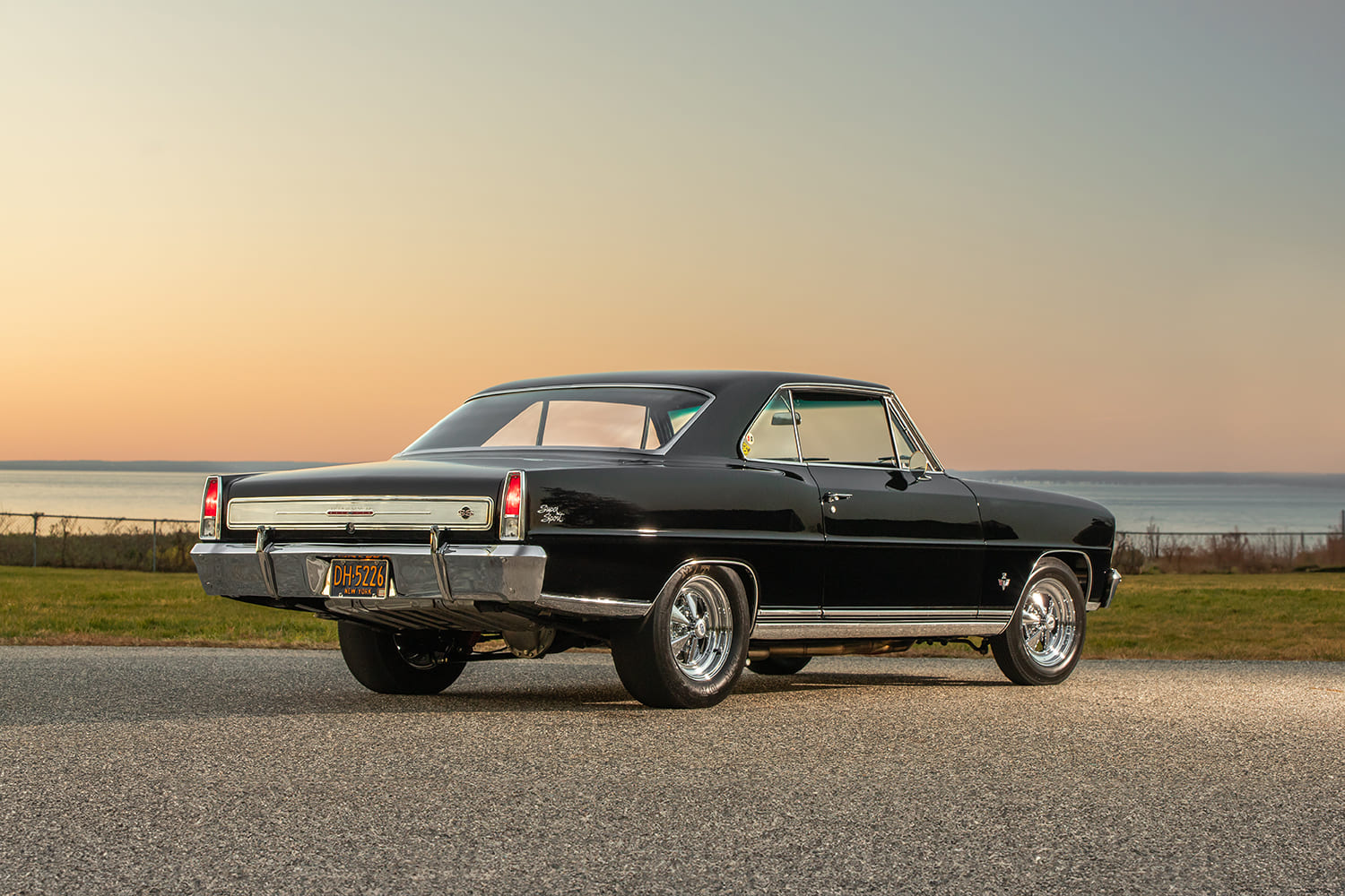 Rear three-quarter perspective of a black 1966 Chevy Nova SS showing polished dual exhaust tips, chrome bumper, and classic five-spoke wheels.