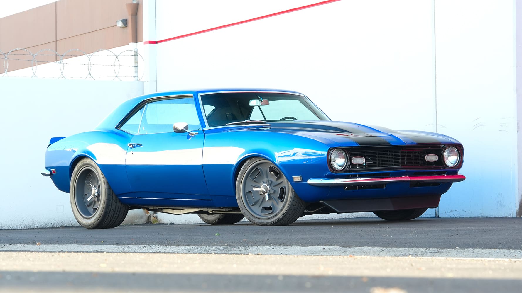 Low-angle front profile showing the lowered pro-touring stance, front air dam, and tucked multi-spoke wheels on a blue 1968 Camaro.