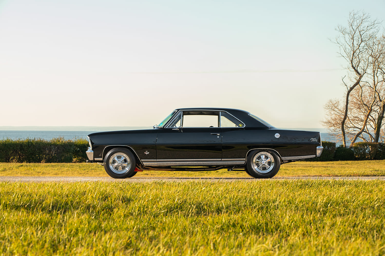 Complete driver-side profile of a lowered 1966 Chevrolet Nova hardtop restomod parked along a rural roadside at golden hour.