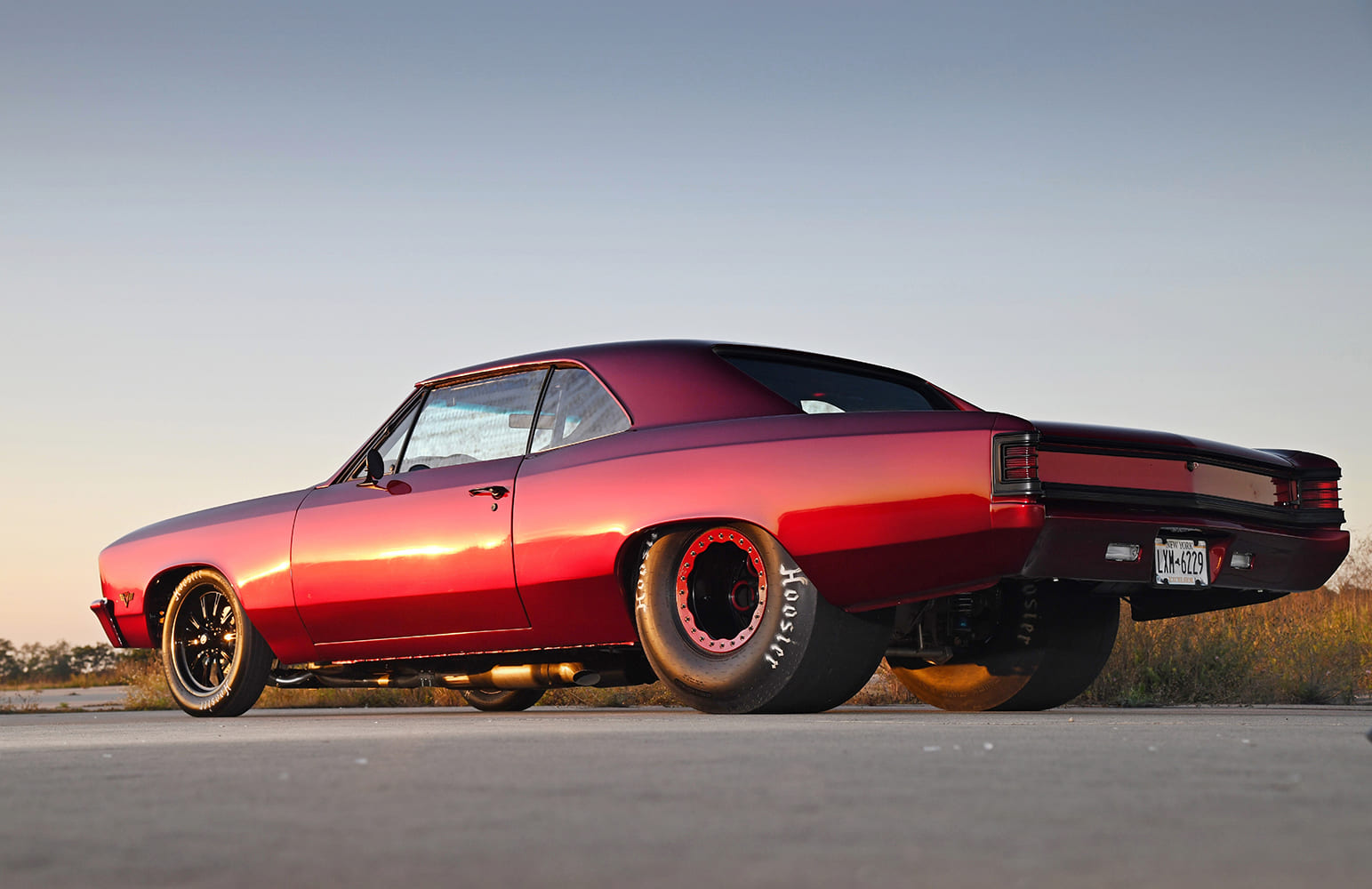 Rear three-quarter low-angle profile of a metallic red big block Chevelle equipped with giant beadlock rear wheels and Hoosier tires.