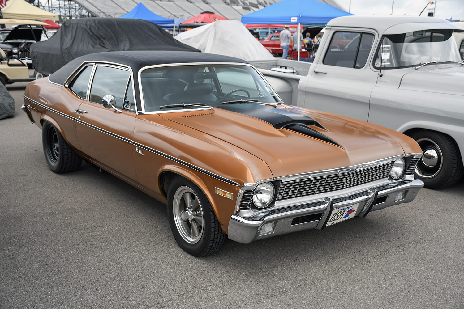 High front three-quarter view of a metallic bronze 1970 Chevy Nova featuring a black vinyl top, custom cowl induction hood, and vintage American Racing wheels.