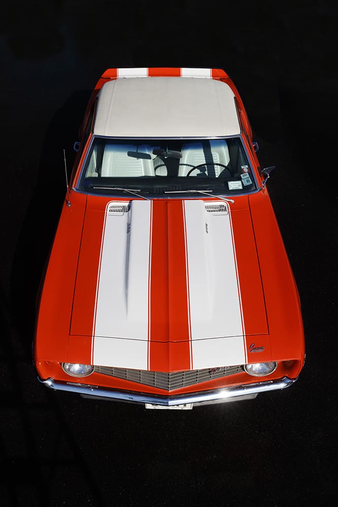 Overhead view facing down over the cowl induction hood and white racing stripes to the grille of an orange 1969 Camaro Z/28.
