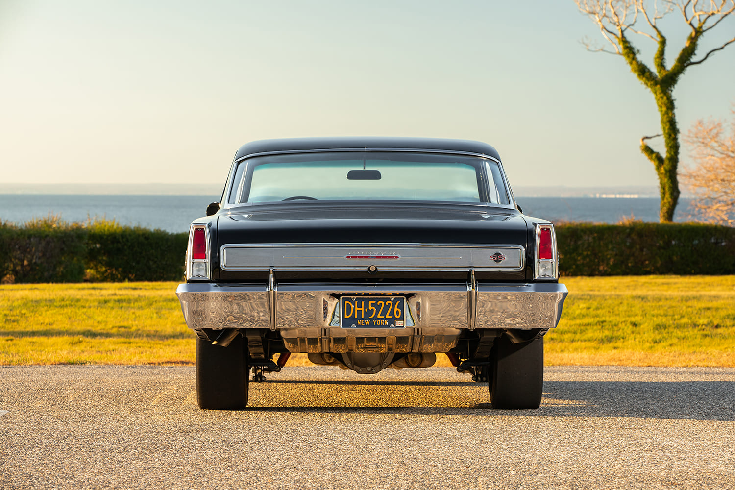 Direct rear-end view of a 1966 Chevy Nova SS showing vertical taillights, brushed trunk panel trim, and classic chrome rear bumper.