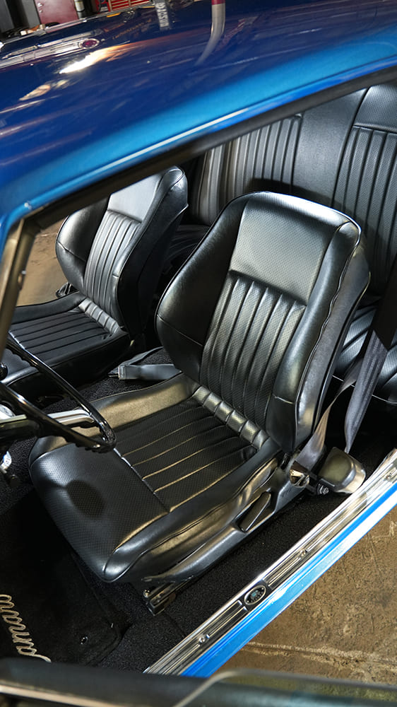 Top-down angle of the high-bolstered black leather front bucket seats and clean black carpeting in a custom 1968 Camaro cabin.