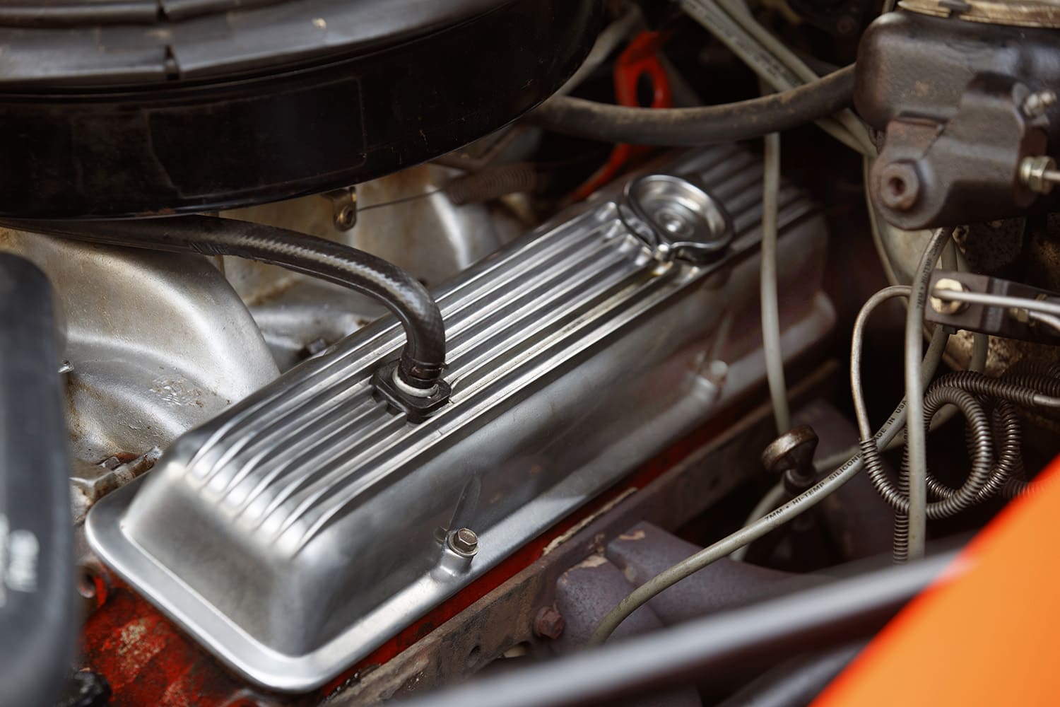 Close-up detail of the factory-ribbed aluminum valve cover, PCV breather hose, and wiring on the driver-side cylinder head of a 302 V8.