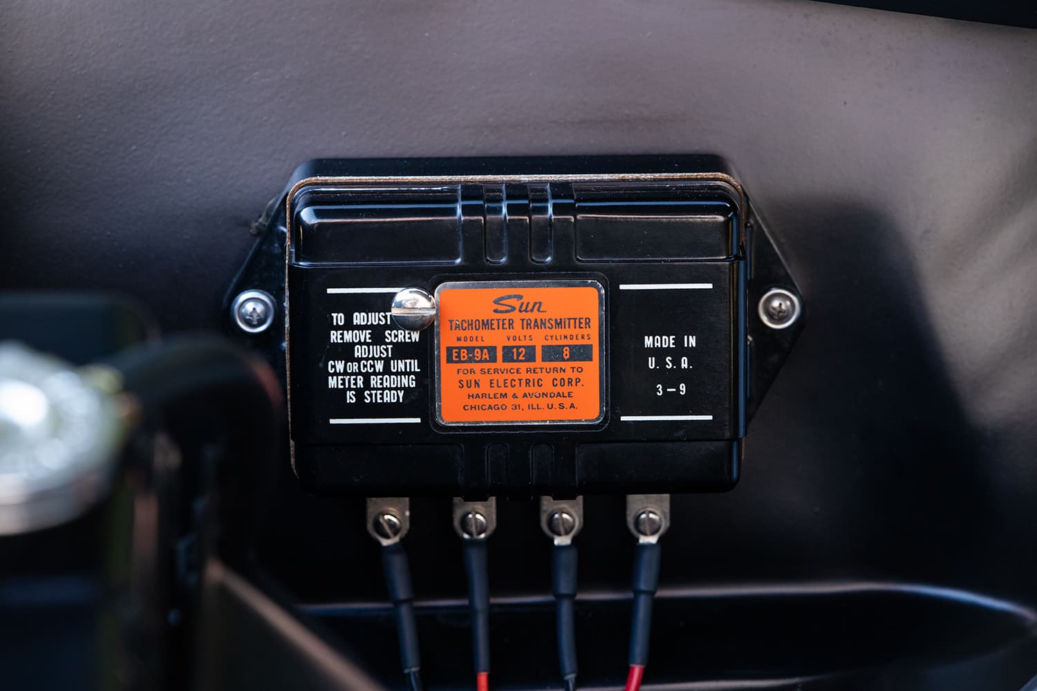 Macro view of a period-correct black Sun EB-9A 12-volt tachometer transmitter box mounted to the inner fender of a classic Chevy Nova.