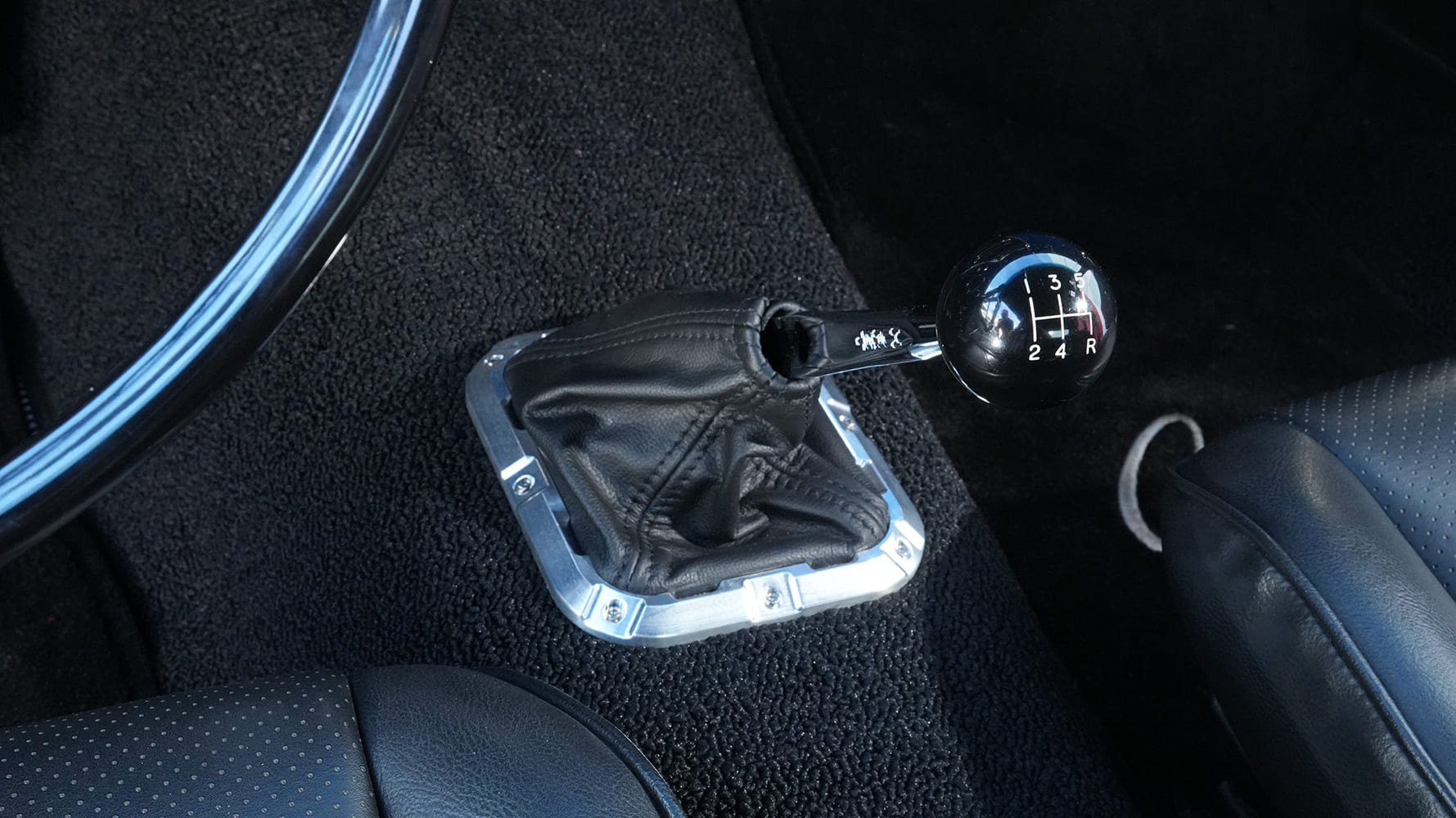 Close-up of a 5-speed pattern shift ball with a leather shift boot and polished billet aluminum trim ring mounted on the floor console.