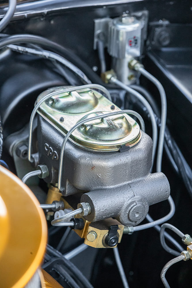 Detailed close-up of a Classic Performance Products cast iron dual-circuit master cylinder with gold-plated caps and hardline plumbing.
