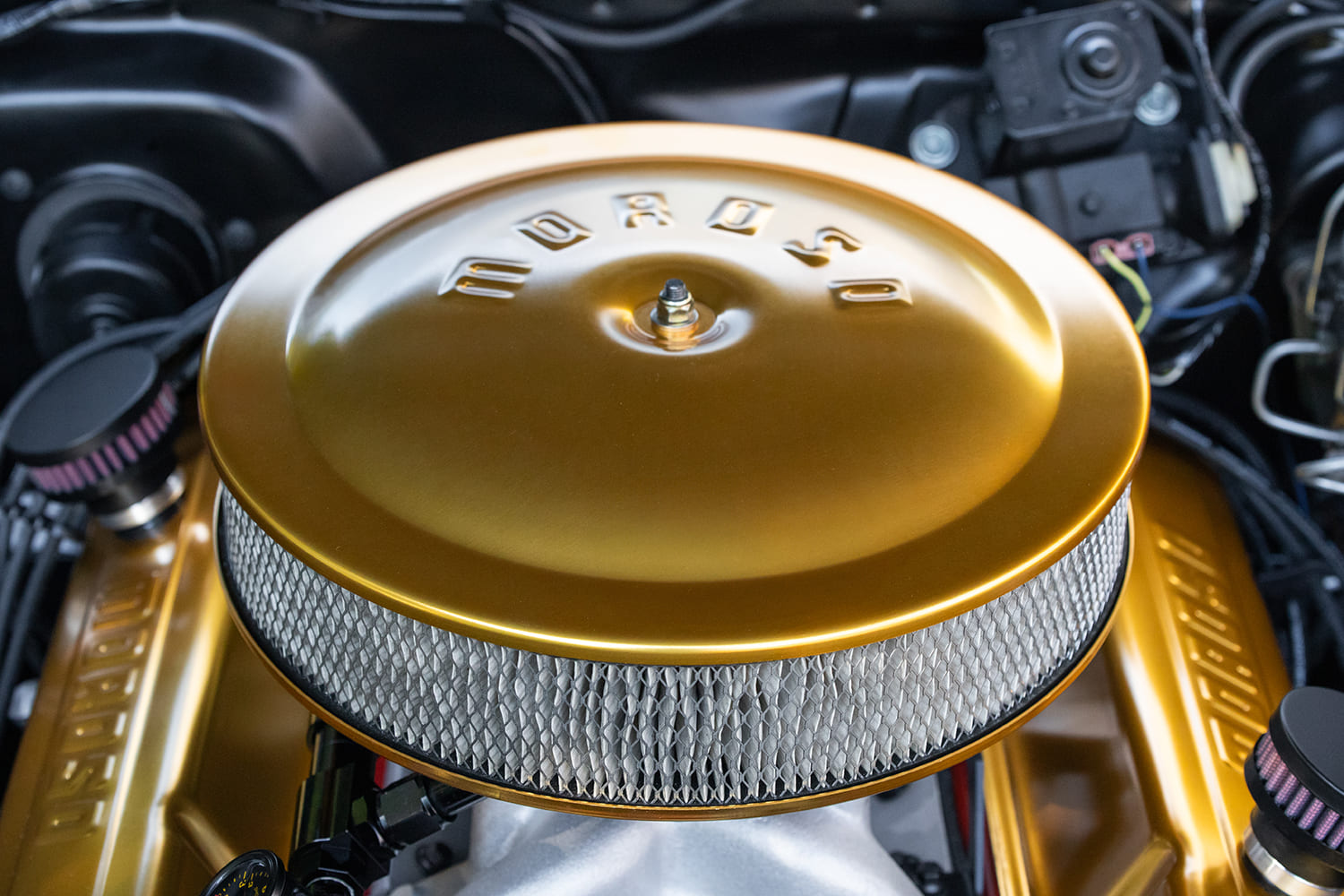 Close-up top angle of a round gold Moroso stamped air cleaner lid with exposed pleated filter element over an aluminum intake manifold.