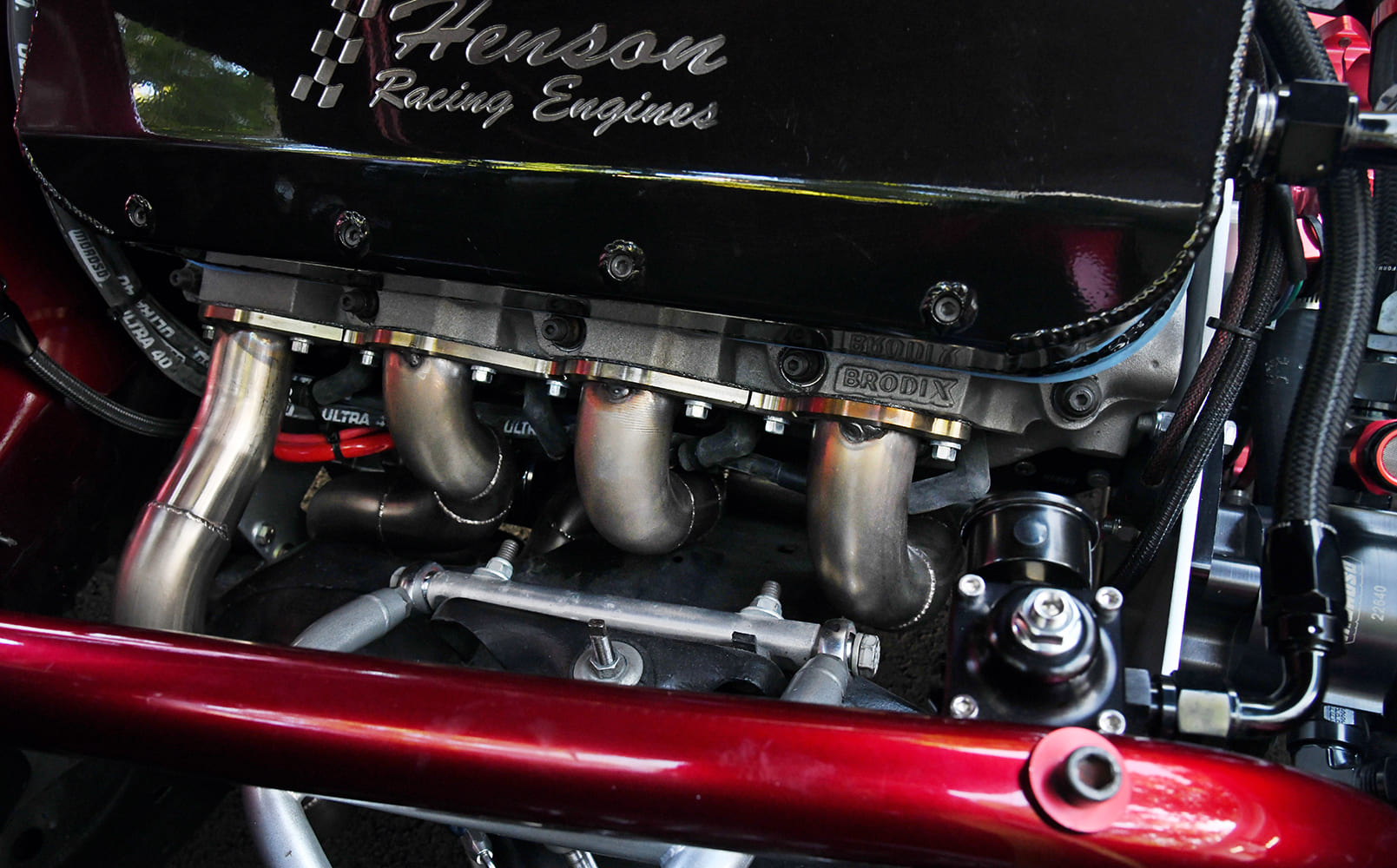 Close-up view of the Brodix aluminum cylinder heads, custom stainless tubular exhaust headers, and red chassis tubework on a Henson Racing engine.