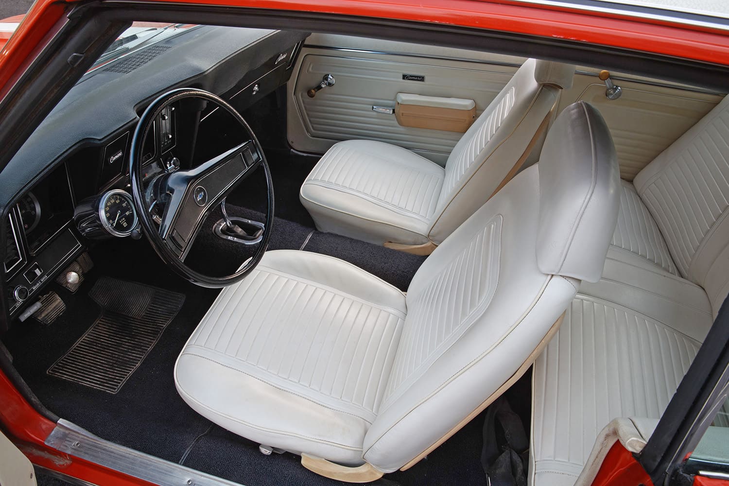 Cockpit view through the open roof of a 1969 Chevrolet Camaro showing unrestored white vinyl high-back bucket seats, steering wheel, and black dashboard.