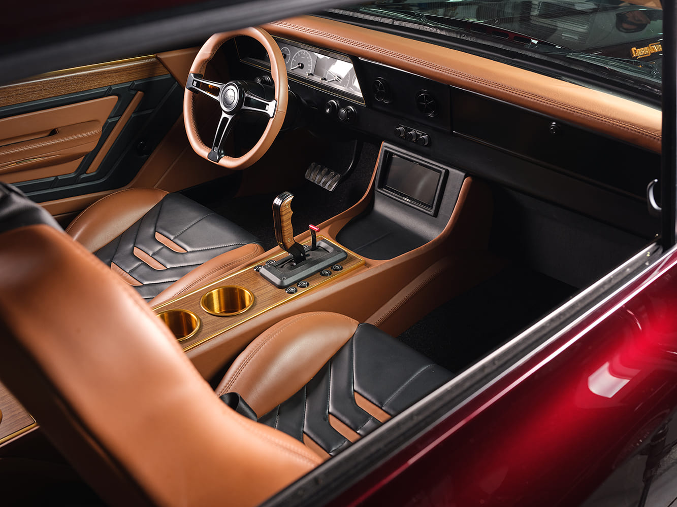 Custom leather interior of the 1967 Chevy Nova Casanova restomod featuring tan and black bolster seats, a Sparco steering wheel, modern touchscreen display, and a gold-accented center console.