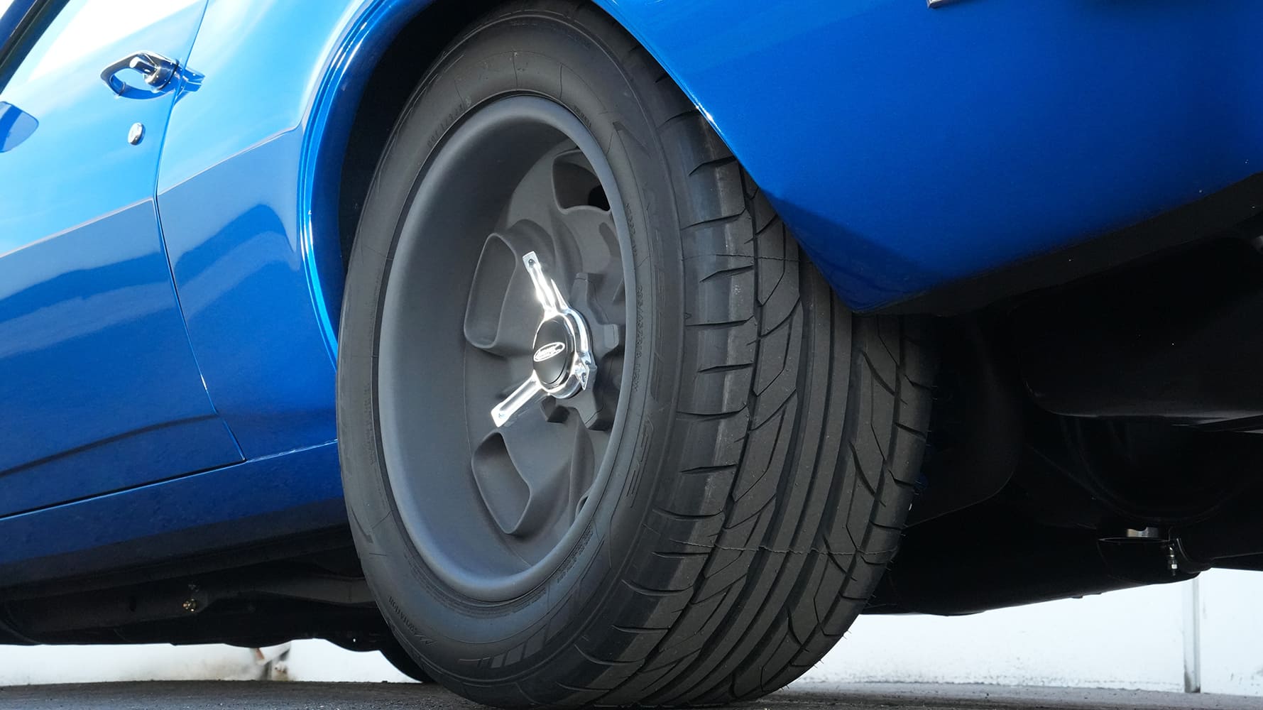 Low-angle close-up of a wide performance tire tucked into the rear fender of a metallic blue 1968 Chevy Camaro street machine.