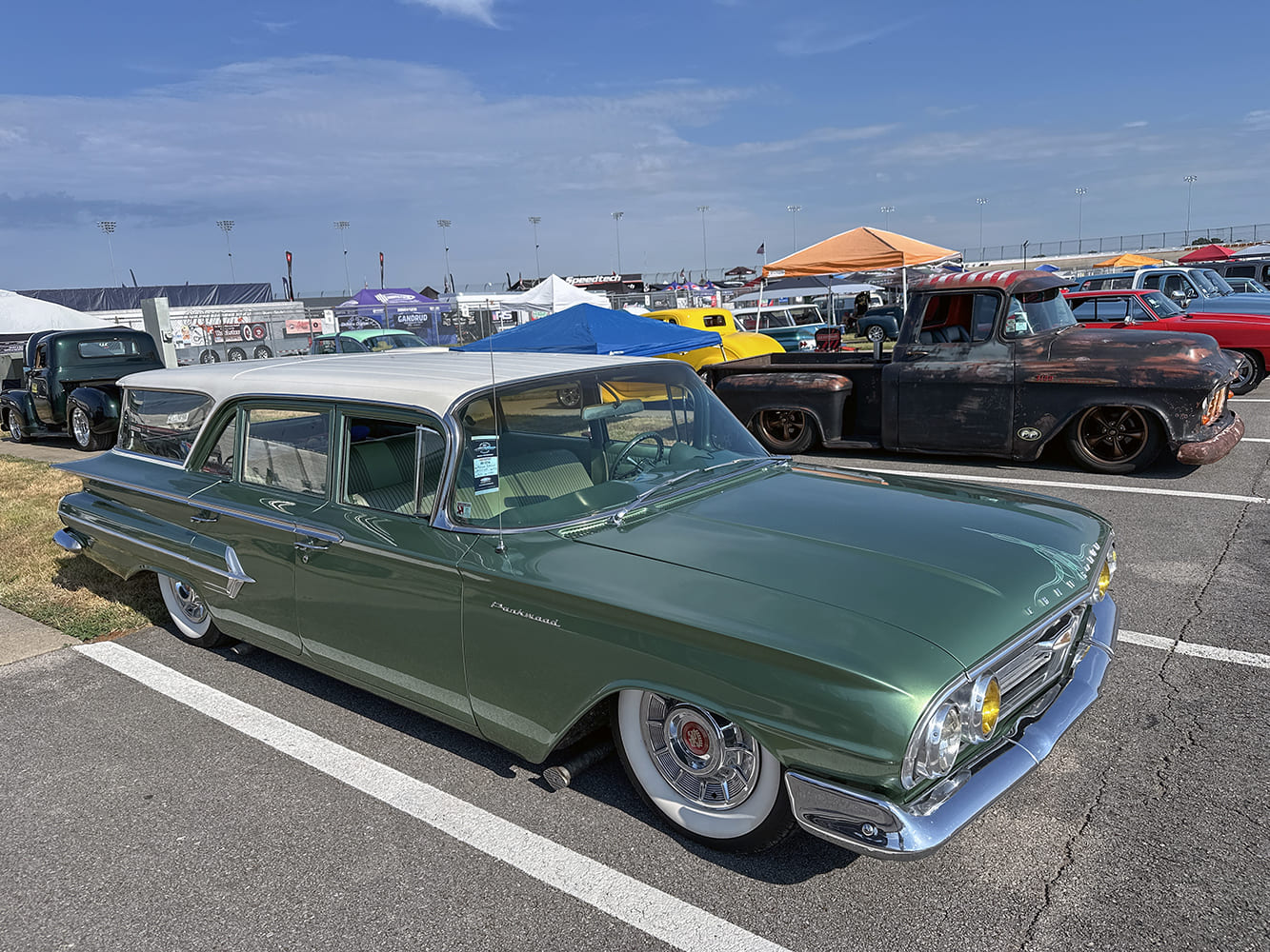 Front three-quarter view of a lowered metallic green 1960 Chevrolet Parkwood station wagon with a white roof and wide whitewall tires parked at an outdoor car show.