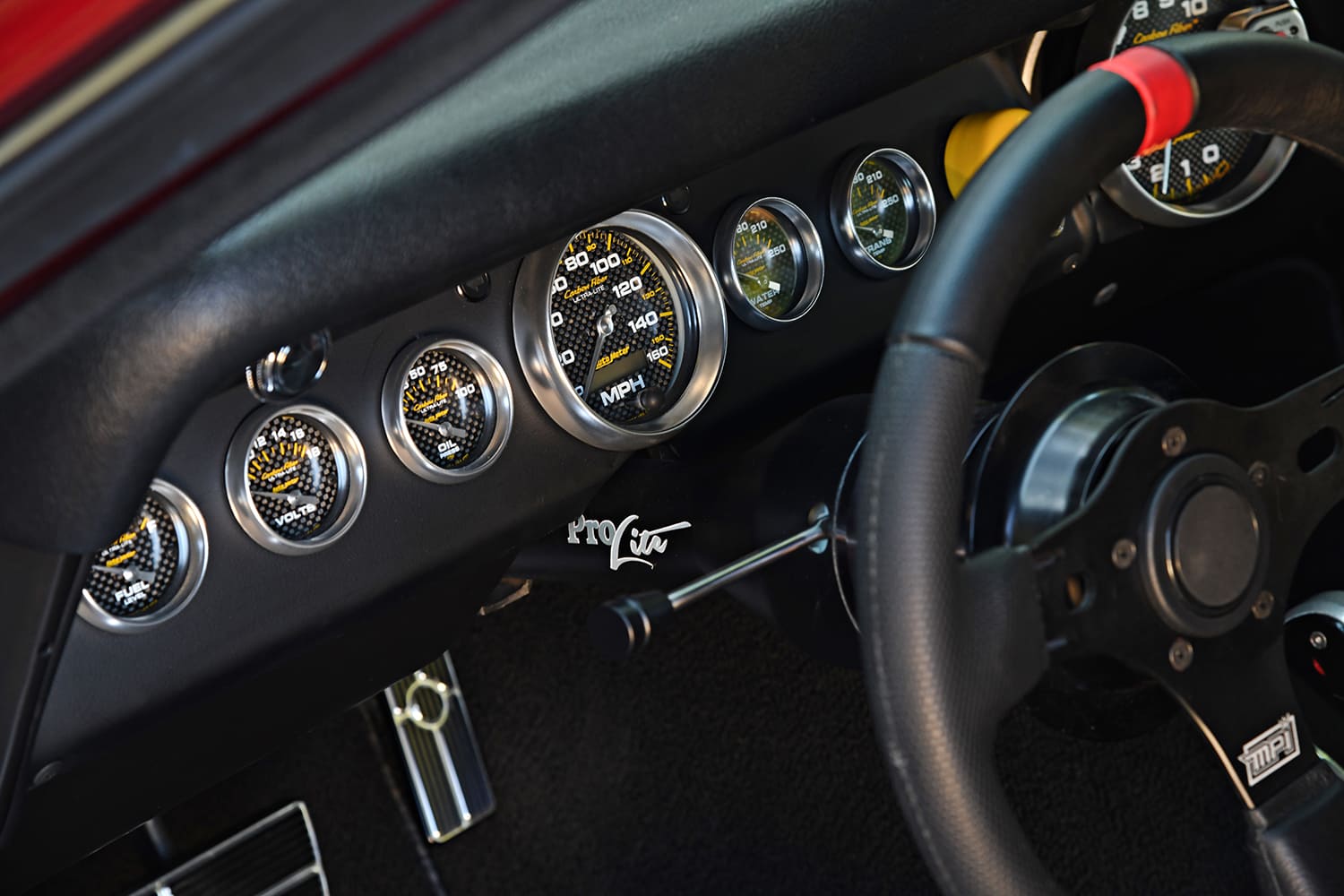Close-up of the black dashboard in a 1967 Big Block Chevelle featuring carbon fiber AutoMeter gauges, custom steering column, and MPI steering wheel.