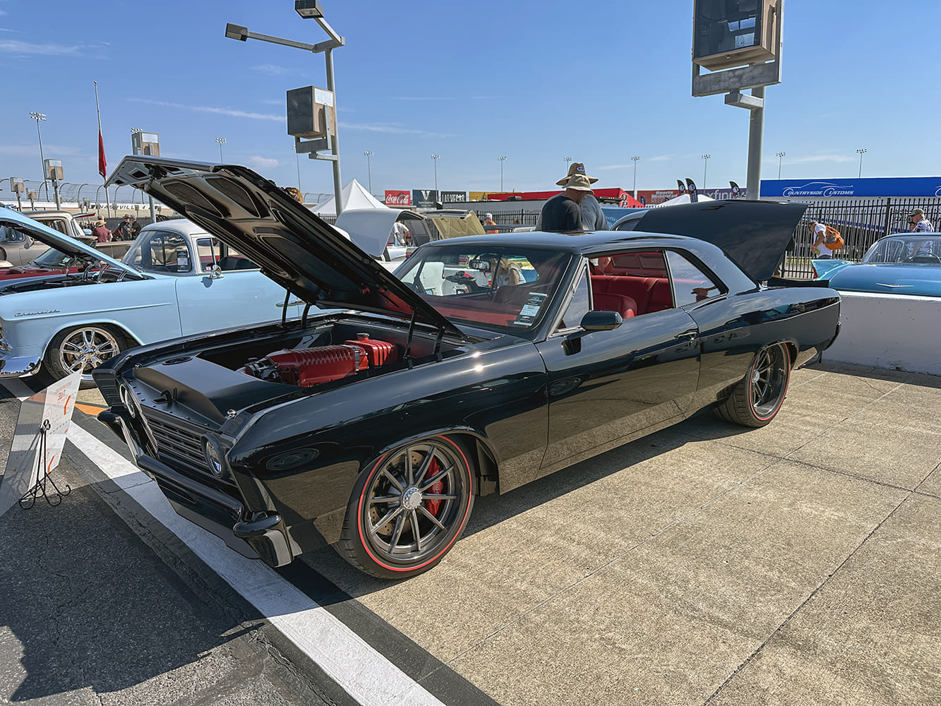 Glossy black 1966 Chevrolet Chevelle restomod with an open hood, red-topped engine, custom wheels with redline tires, and open trunk lid.