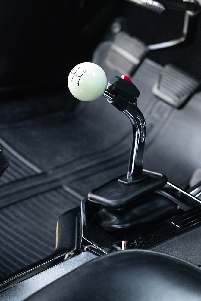 Close-up of a chrome manual floor shifter topped with a white cue-ball four-speed shift knob and integrated red line-lock launch button.