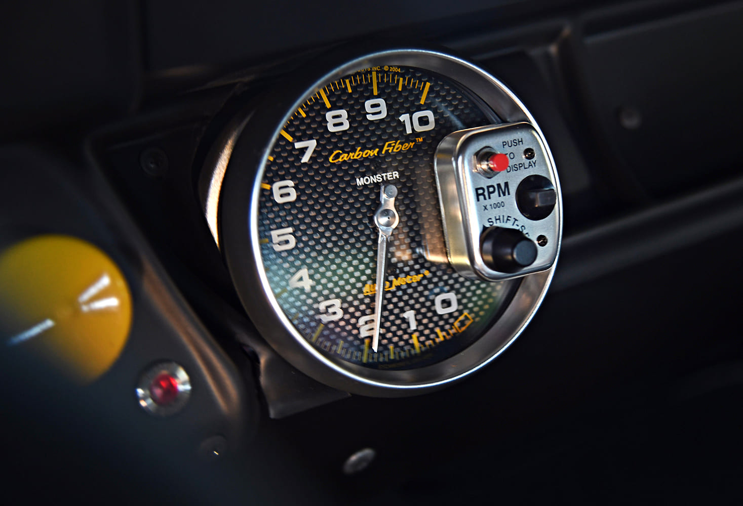 Detailed view of an AutoMeter Carbon Fiber series Monster tachometer with an integrated shift light and RPM recall display mounted on the dash.