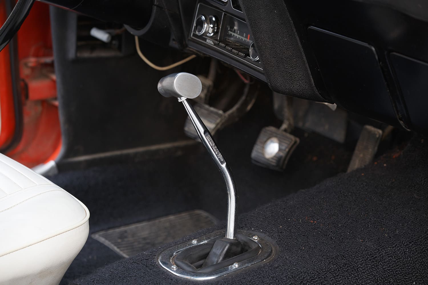 Chrome Hurst competition floor shifter equipped with a brushed aluminum T-handle grip rising from the black carpeted transmission tunnel.