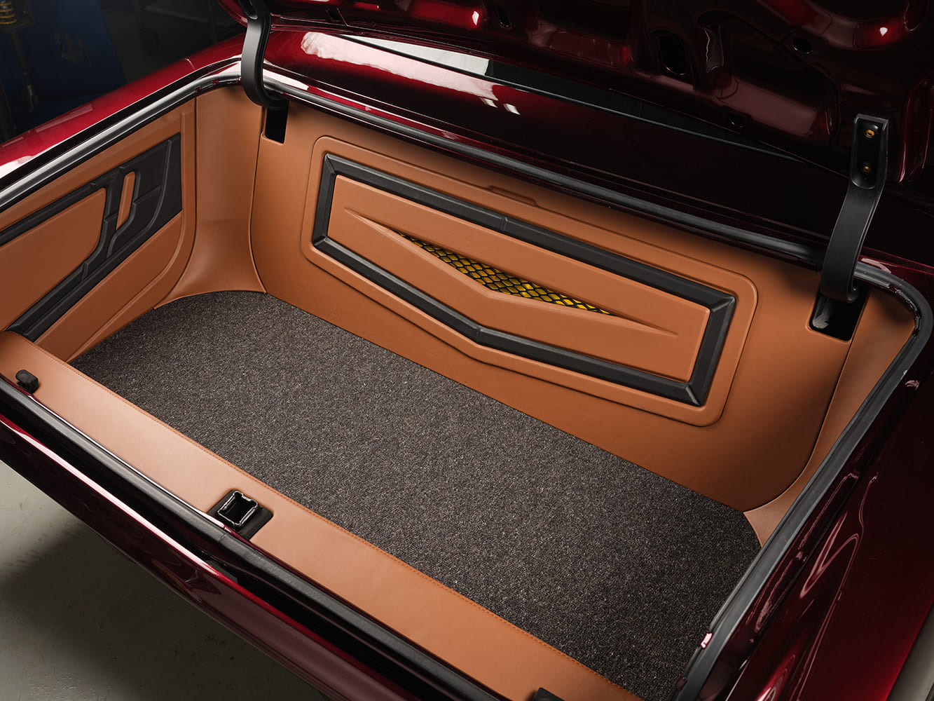 Fully finished trunk interior of the 1967 Chevy Nova restomod lined with tan leather panels, charcoal carpeting, and a custom accent grille insert.