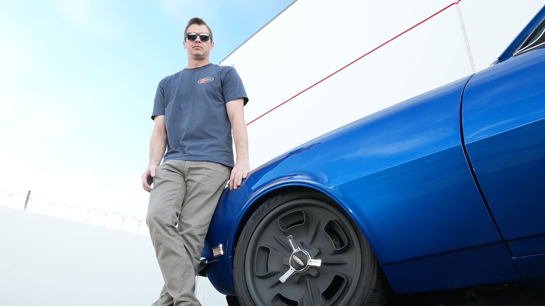 Car owner leaning against the front fender of a custom lowered blue 1968 Chevrolet Camaro pro-touring build.