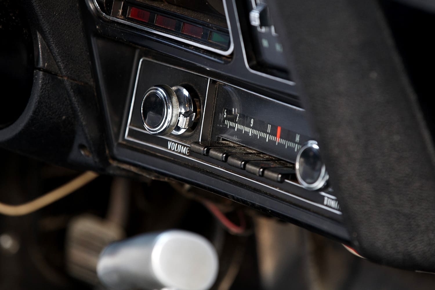 Detailed view of the unrestored Delco AM pushbutton radio unit and heater controls set into the textured black plastic dashboard bezel.