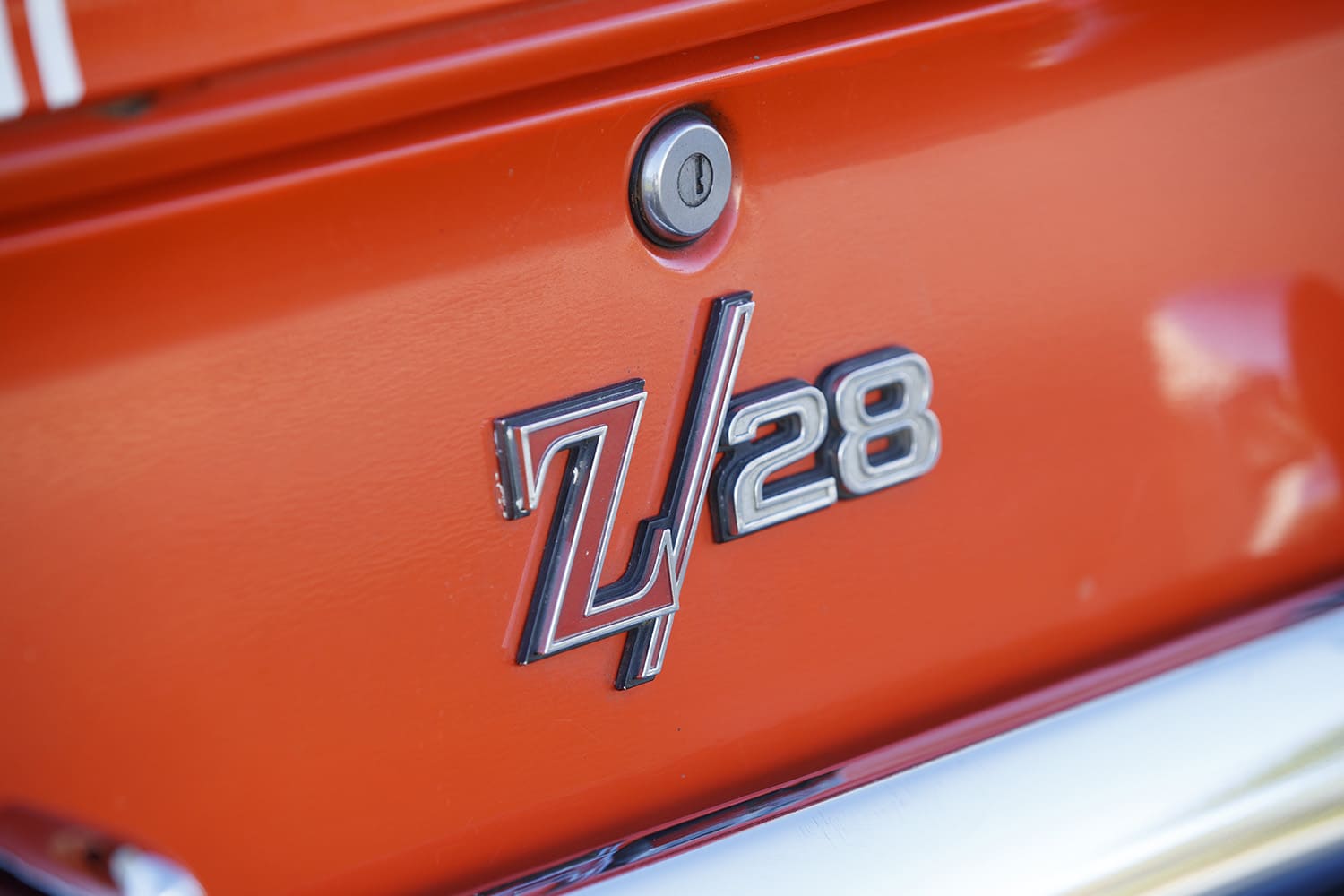 Macro detail of the chrome-bordered Z/28 emblem mounted beside the trunk key lock cylinder on the Hugger Orange rear decklid.