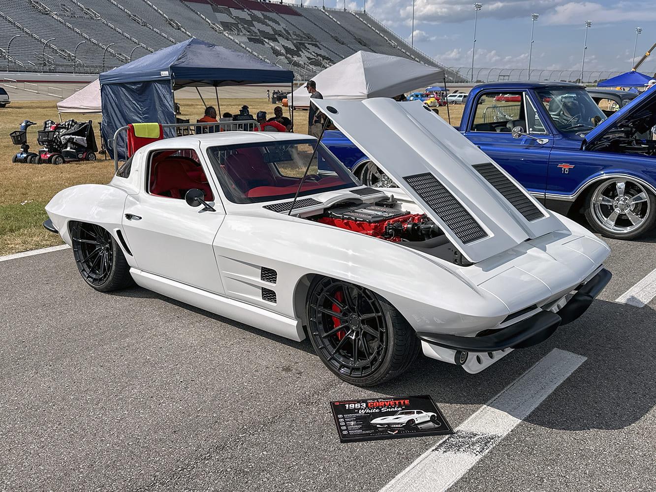 Front three-quarter ground view of a widebody white 1963 Chevrolet Corvette restomod with an open cowl hood showing an LT V8 engine and black wheels
