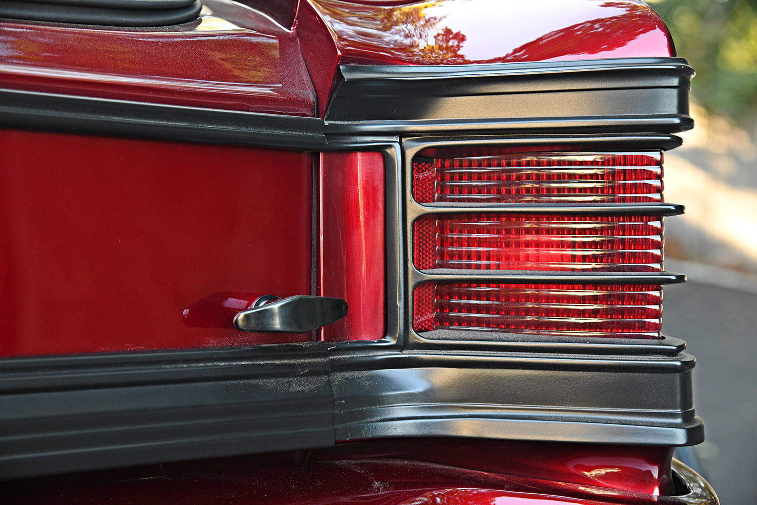 Detail view of the custom satin black taillight bezel, ribbed red lens, and trunk latch assembly on a metallic red 1967 Chevelle.