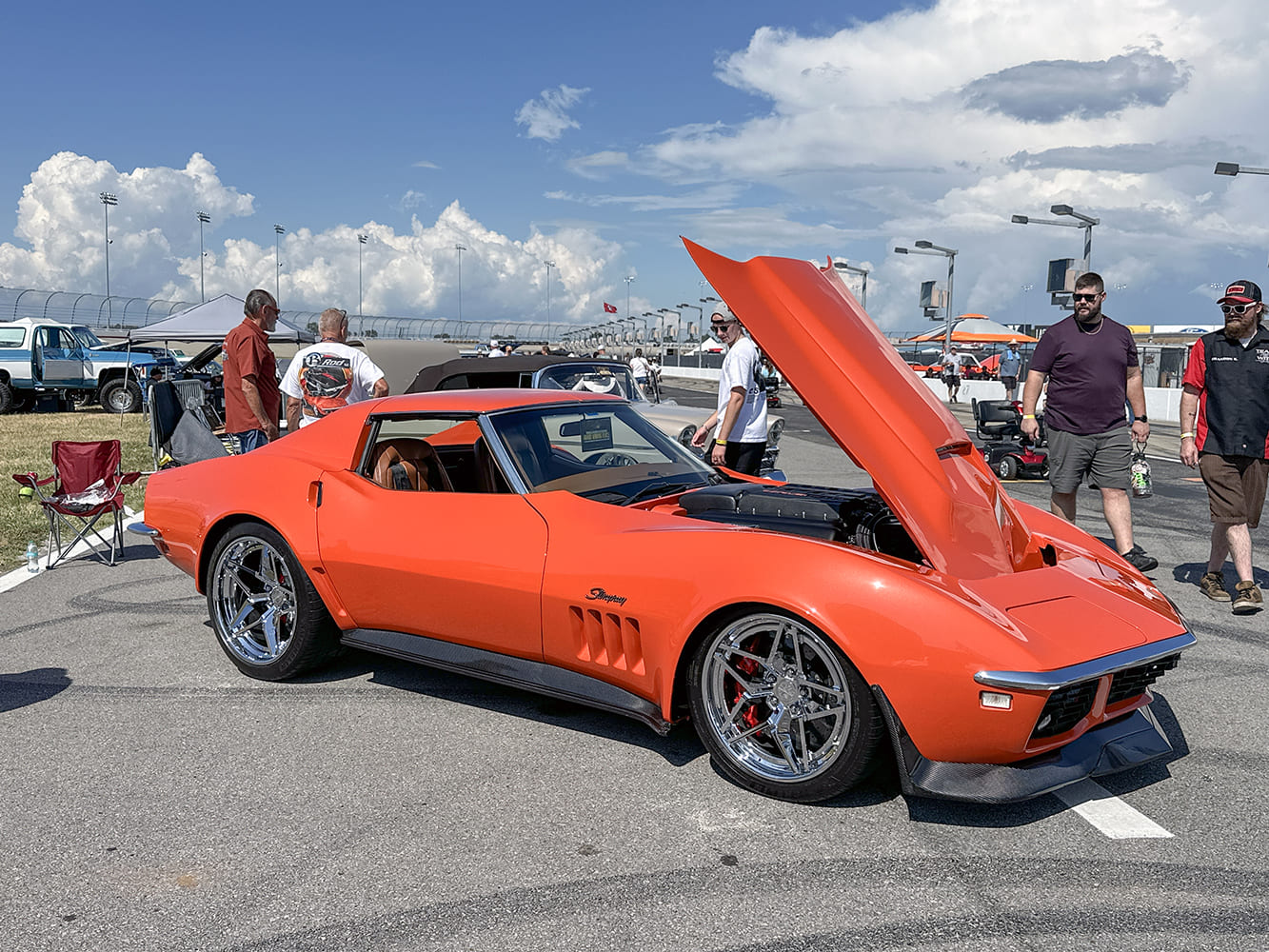 Front three-quarter view of a bright orange 1969 Corvette C3 with a forward-tilt hood, modern LT engine, carbon fiber ground effects, and chrome wheels.