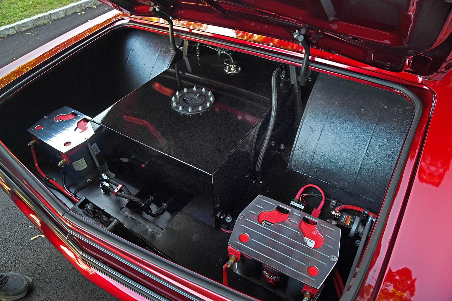 Open trunk layout of a 1967 Chevelle showing tubbed wheel wells, a gloss black racing fuel cell, and dual Optima batteries in billet mounts.