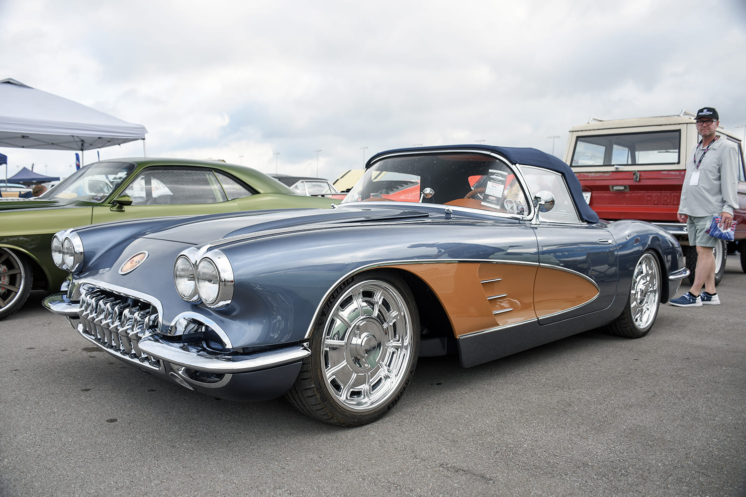 Low front three-quarter view of a custom steel-blue 1958 Corvette roadster with copper coves, chrome tooth grille, and large modern billet wheels.