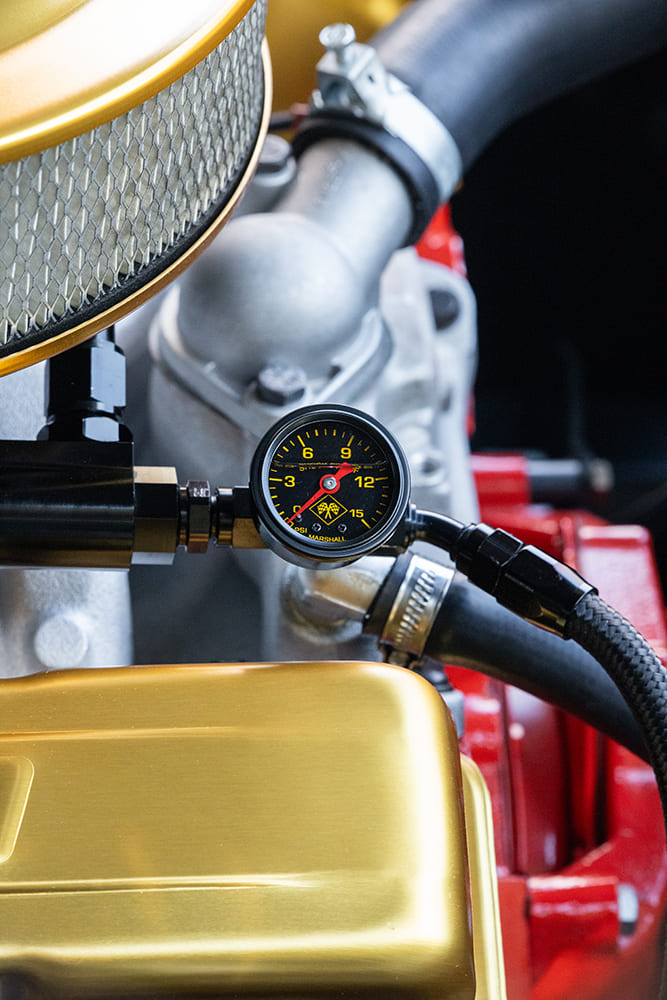 Close-up of an inline Marshall 0-15 PSI fuel pressure gauge with black braided lines mounted above gold-anodized valve covers.