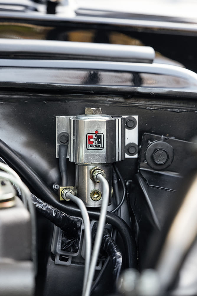 Close-up of an inline Marshall 0-15 PSI fuel pressure gauge with black braided lines mounted above gold-anodized valve covers.