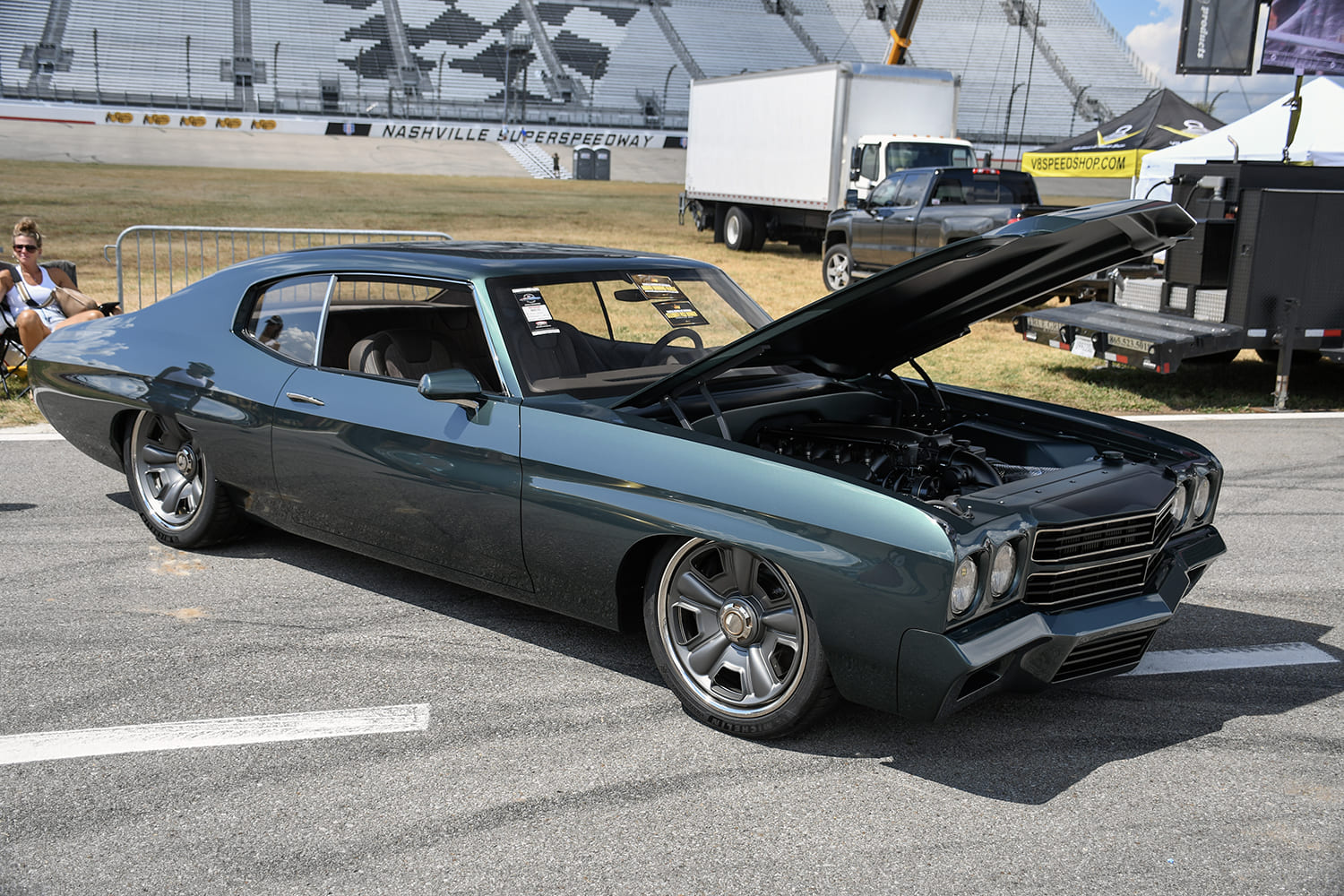 Low-angle front three-quarter profile of a deep gunmetal green 1970 Chevrolet Chevelle restomod with an open hood, custom modern wheels, and lowered stance.