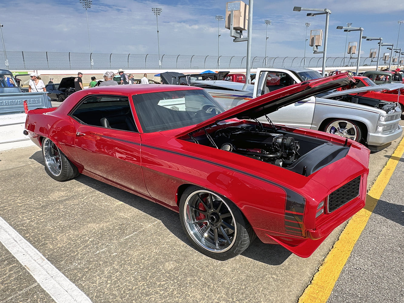 Front-end view of a gloss candy apple red 1969 Chevrolet Camaro restomod with an open cowl-induction hood, black custom front grille, and modern performance wheels.