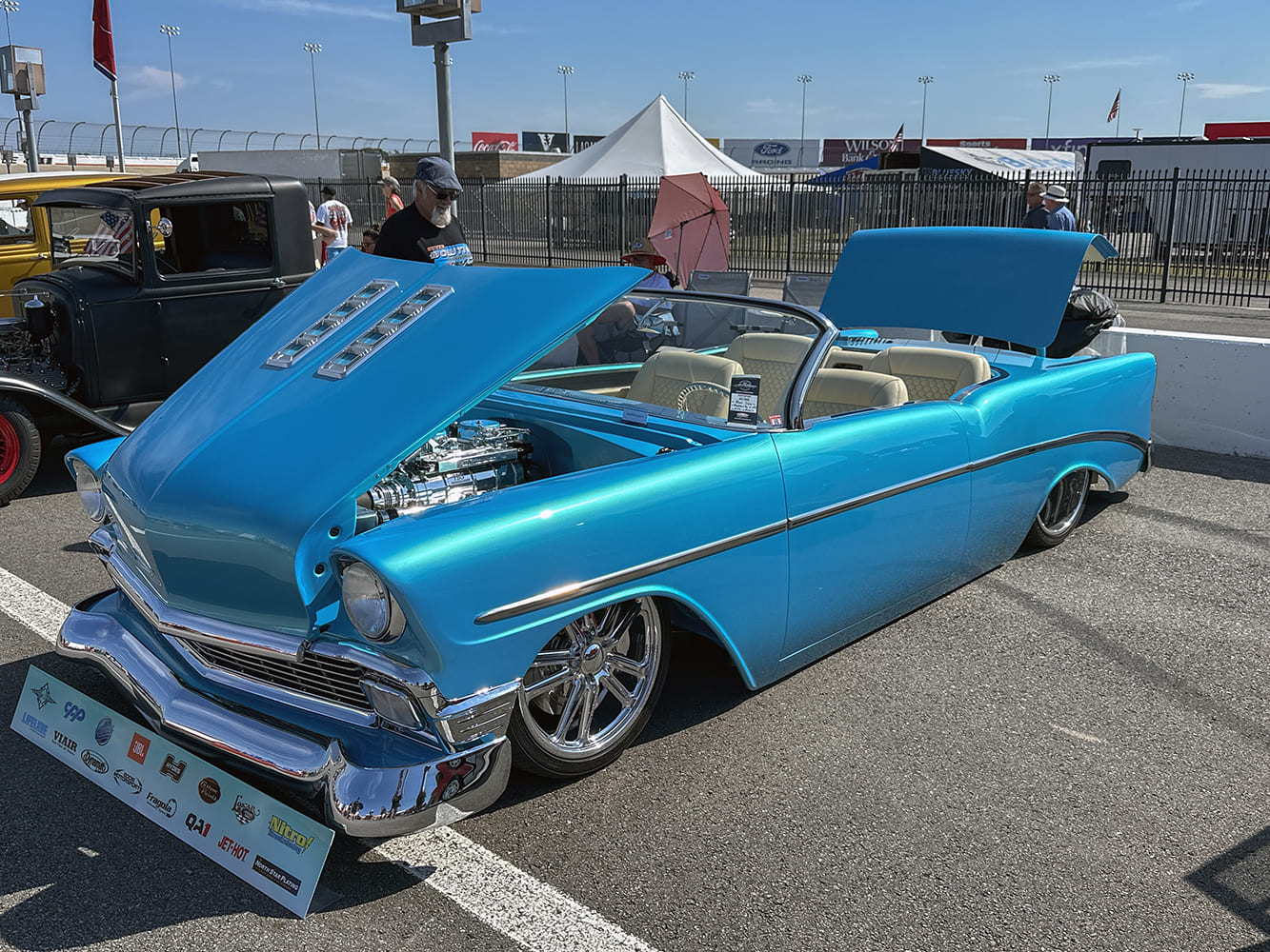 High front three-quarter view of an electric turquoise 1956 Chevy Bel Air custom roadster with shaved door handles, a chopped windshield, custom interior, and chrome wheels.