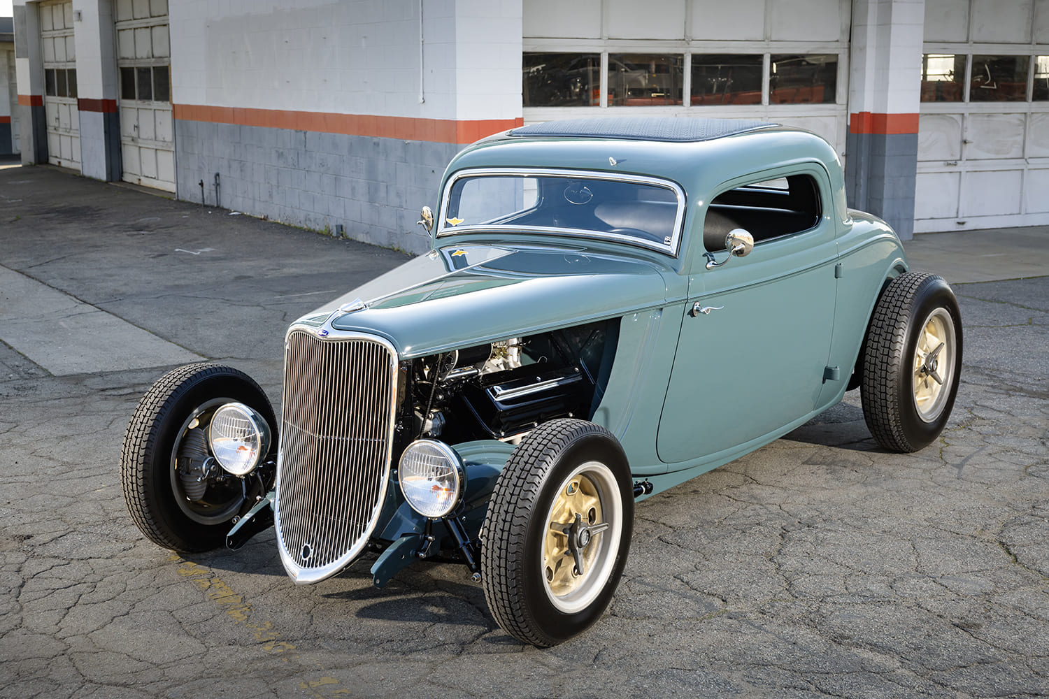Low-angle front view of a slate blue-teal chopped 1933 Ford 3-Window Coupe highlighting the exposed front suspension and open engine bay.