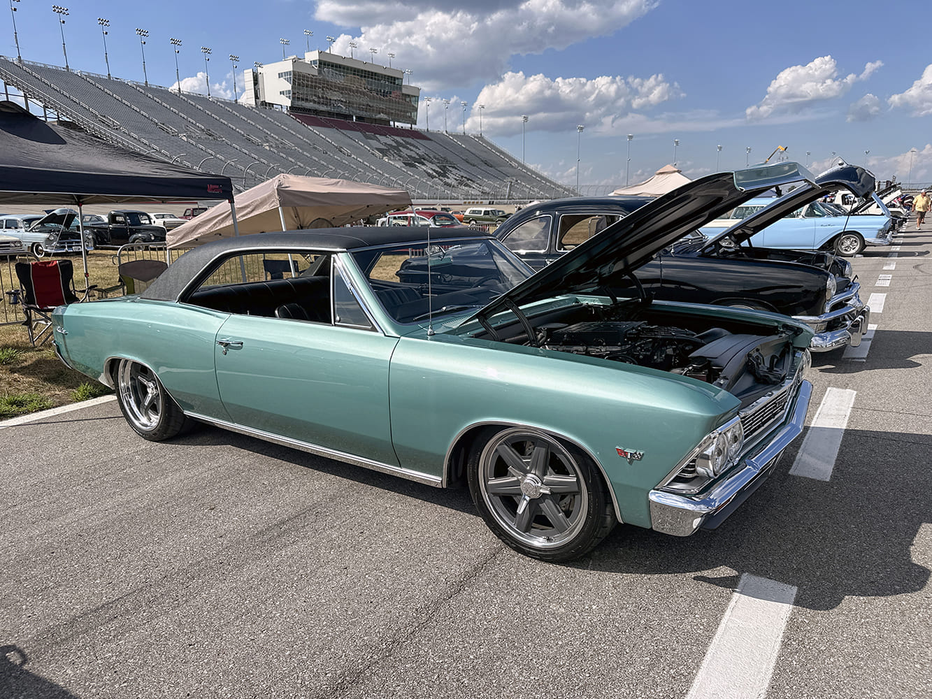 Front three-quarter view of a lowered seafoam green 1966 Chevrolet Chevelle with a black vinyl hardtop, open hood, and modern gray five-spoke alloy wheels.