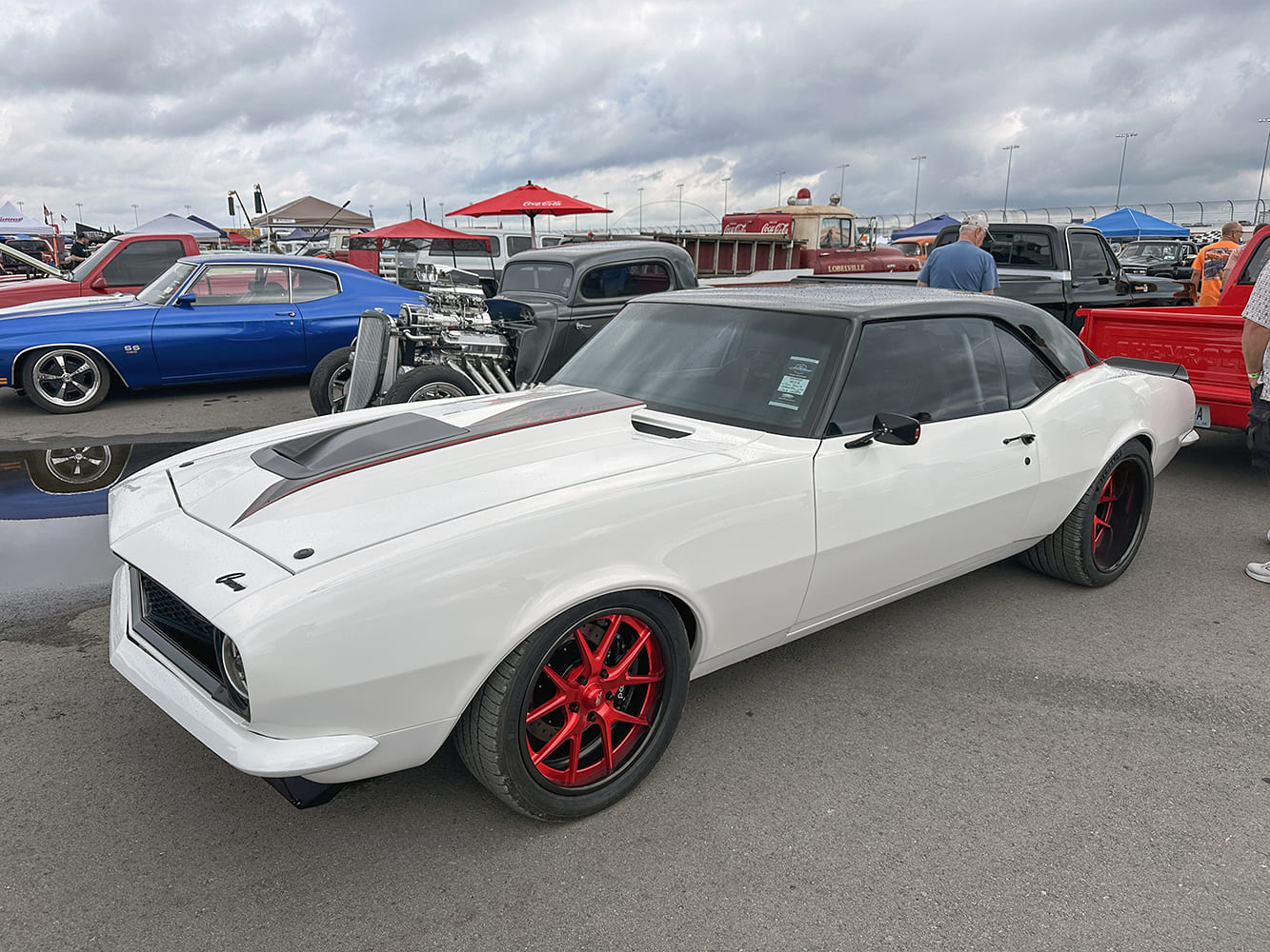 Front three-quarter angle of a custom white 1968 Chevrolet Camaro featuring a dark gray roof, cowl-induction hood scoop, and bright red wheels.