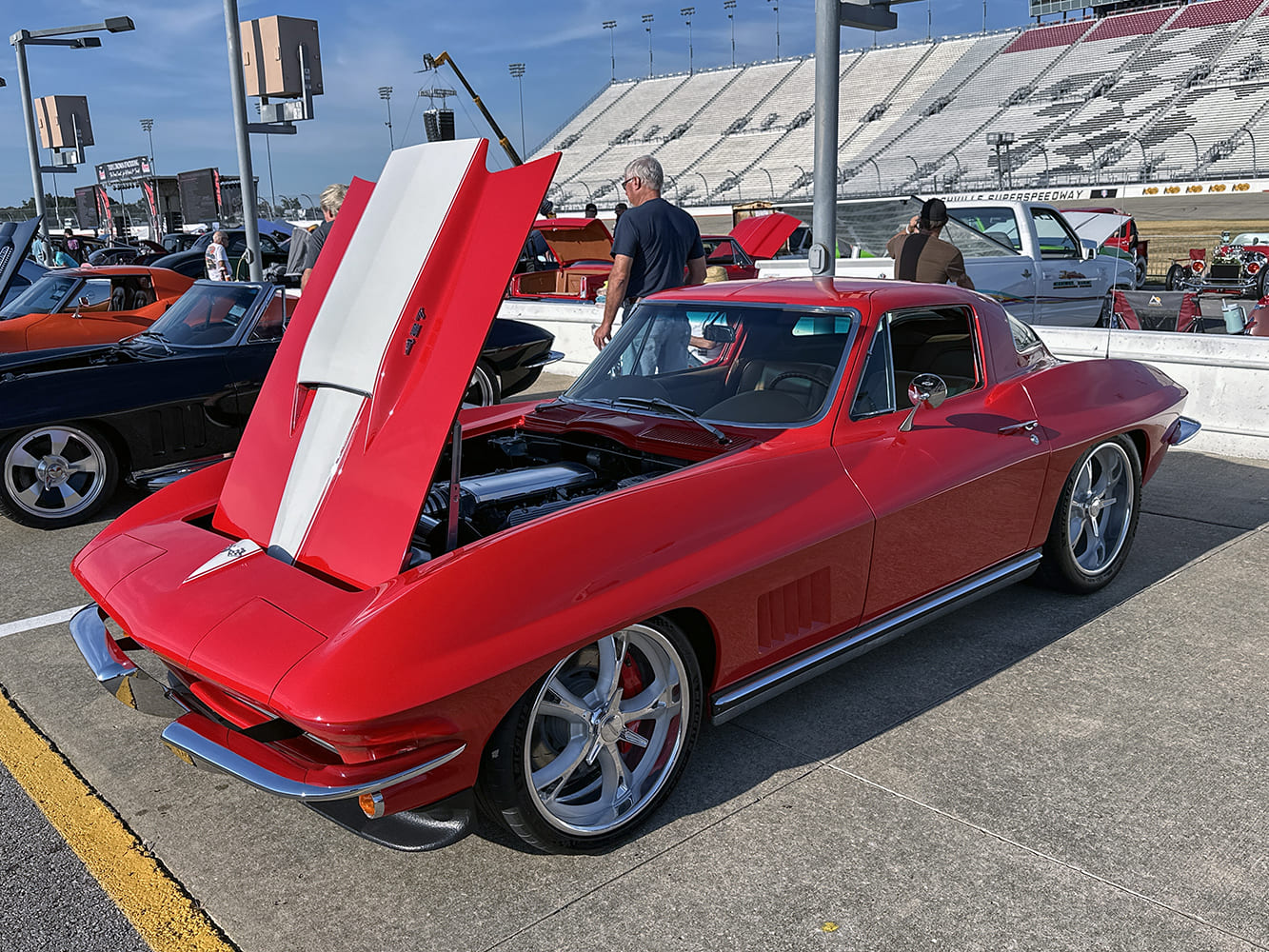 Front three-quarter view of a bright red 1967 Corvette C2 coupe with an open white stinger hood revealing a modern V8 engine and polished wheels
