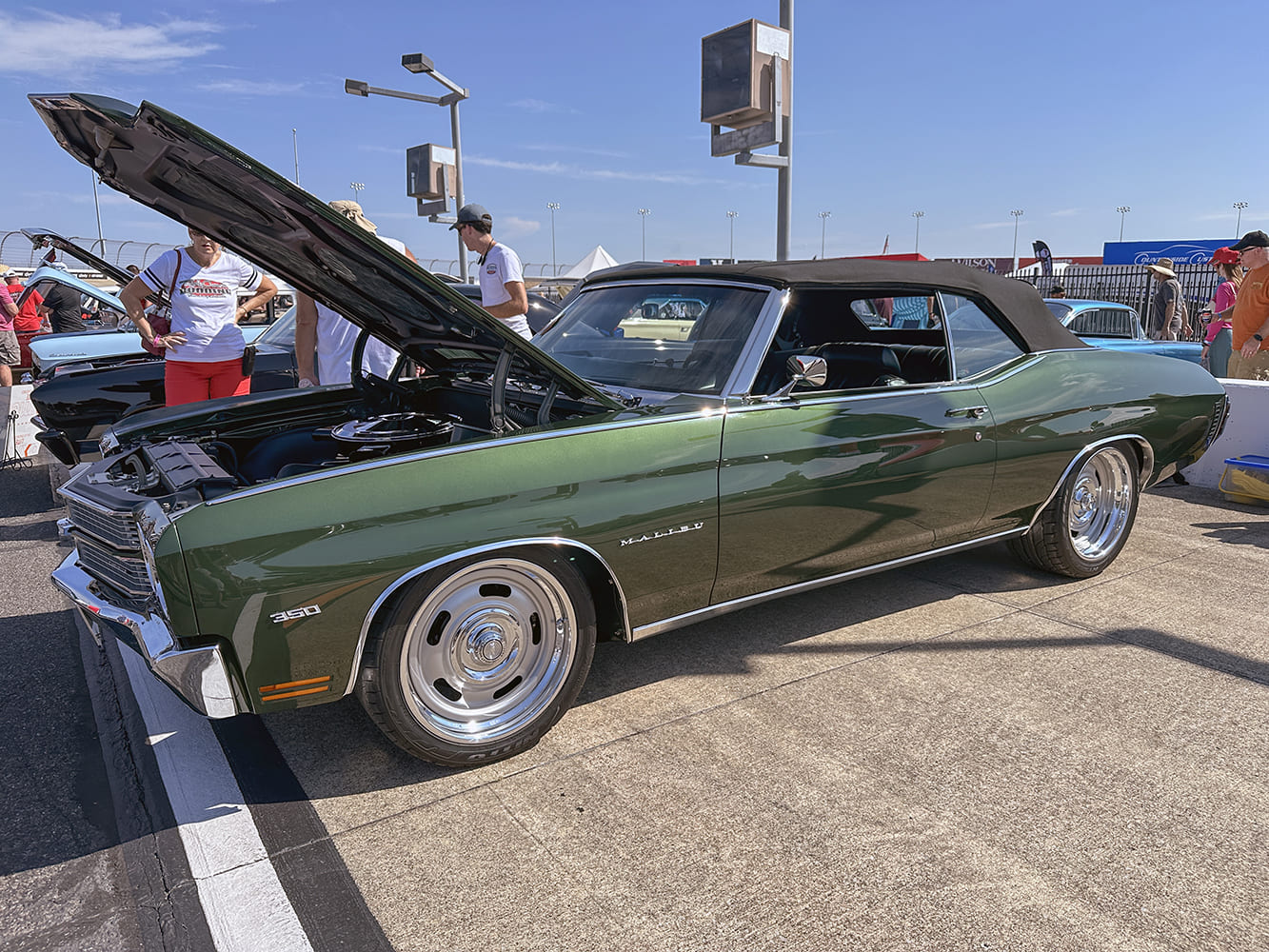 Side three-quarter profile of a forest green metallic 1970 Chevrolet Chevelle Malibu convertible with chrome rally wheels and an open hood.