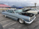 The 4th Annual Triple Crown of Rodding Car Show Low front three-quarter view of a slammed slate-blue 1963 Chevrolet Impala hardtop with an open hood, chrome grille, and large polished wheels.
