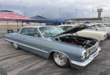 The 4th Annual Triple Crown of Rodding Car Show Low front three-quarter view of a slammed slate-blue 1963 Chevrolet Impala hardtop with an open hood, chrome grille, and large polished wheels.