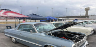 Low front three-quarter view of a slammed slate-blue 1963 Chevrolet Impala hardtop with an open hood, chrome grille, and large polished wheels.