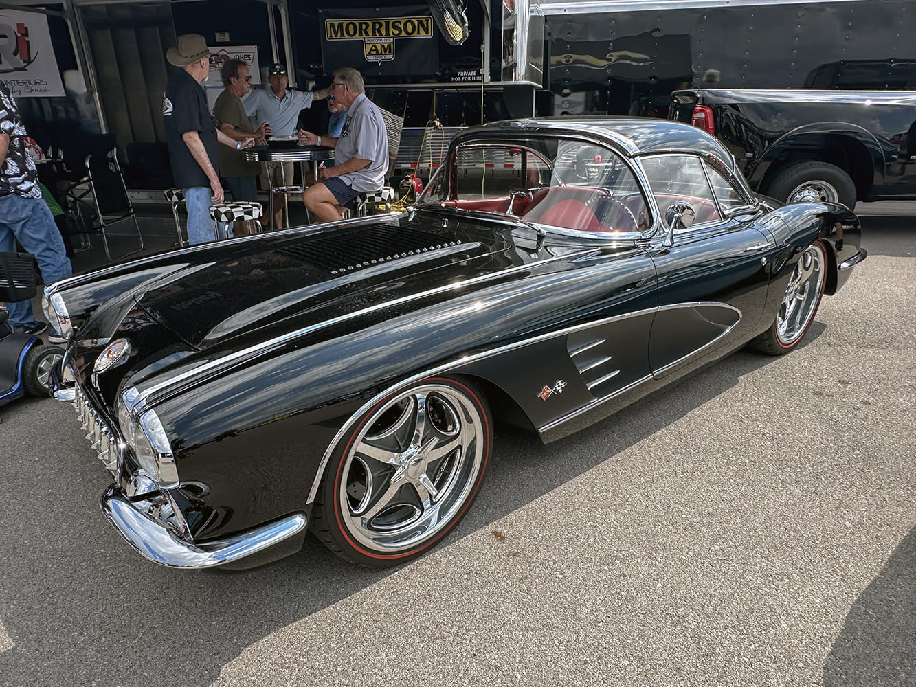 Front three-quarter view of a high-gloss black 1959 Chevrolet Corvette convertible with red interior, chrome hardtop, and modern multi-spoke redline wheels.