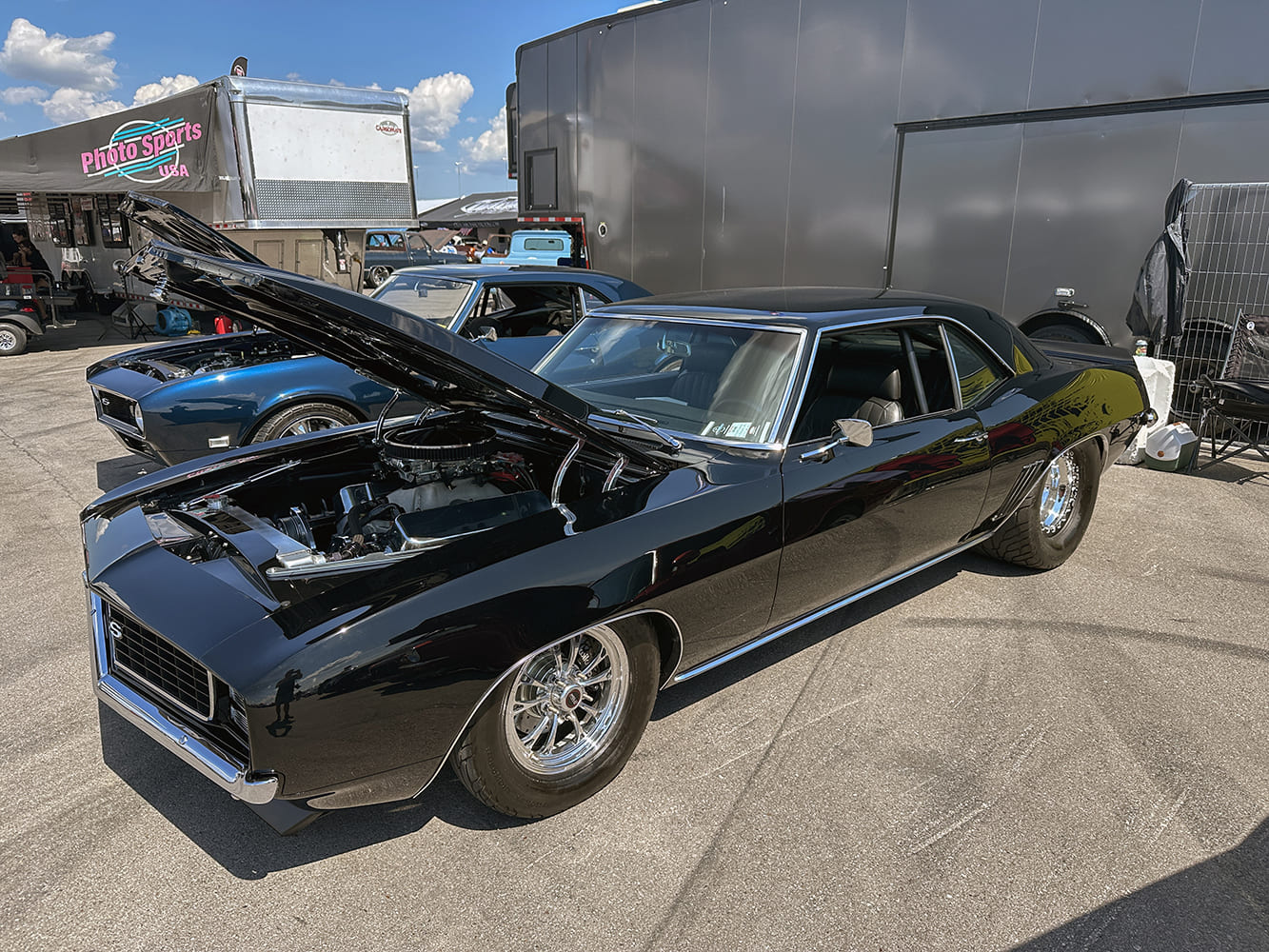 Gloss black 1969 Chevrolet Camaro RS with a cowl-induction hood open, polished Weld-style drag wheels, and large rear slicks parked outside a trailer.