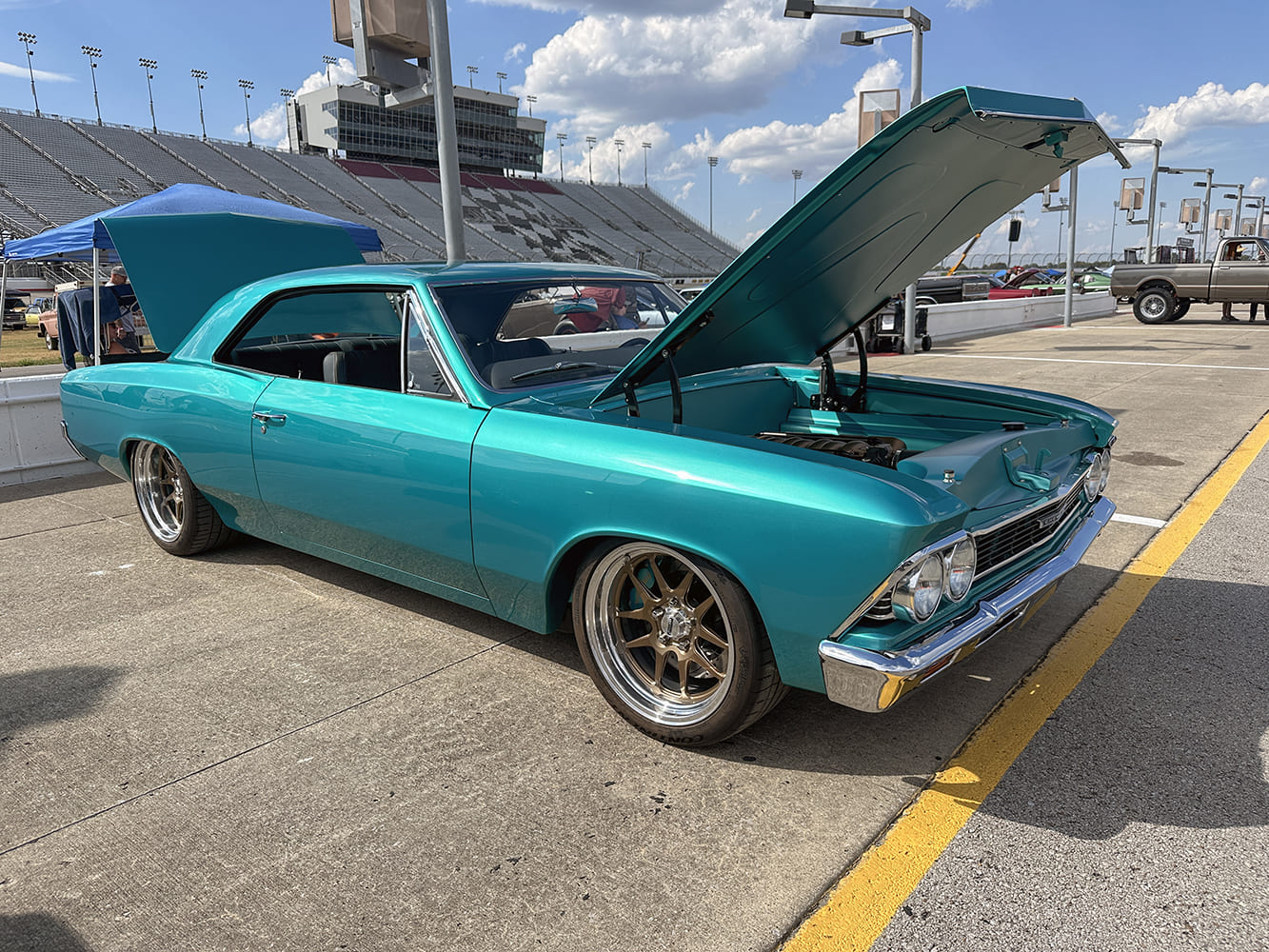 Front three-quarter view of a bright teal 1966 Chevrolet Chevelle hardtop with an open hood, bronze-center wheels, and lowered pro-touring stance