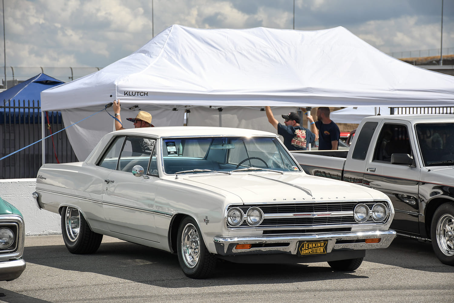 Front three-quarter view of a clean off-white 1965 Chevrolet Chevelle Malibu hardtop parked in front of a white event canopy.